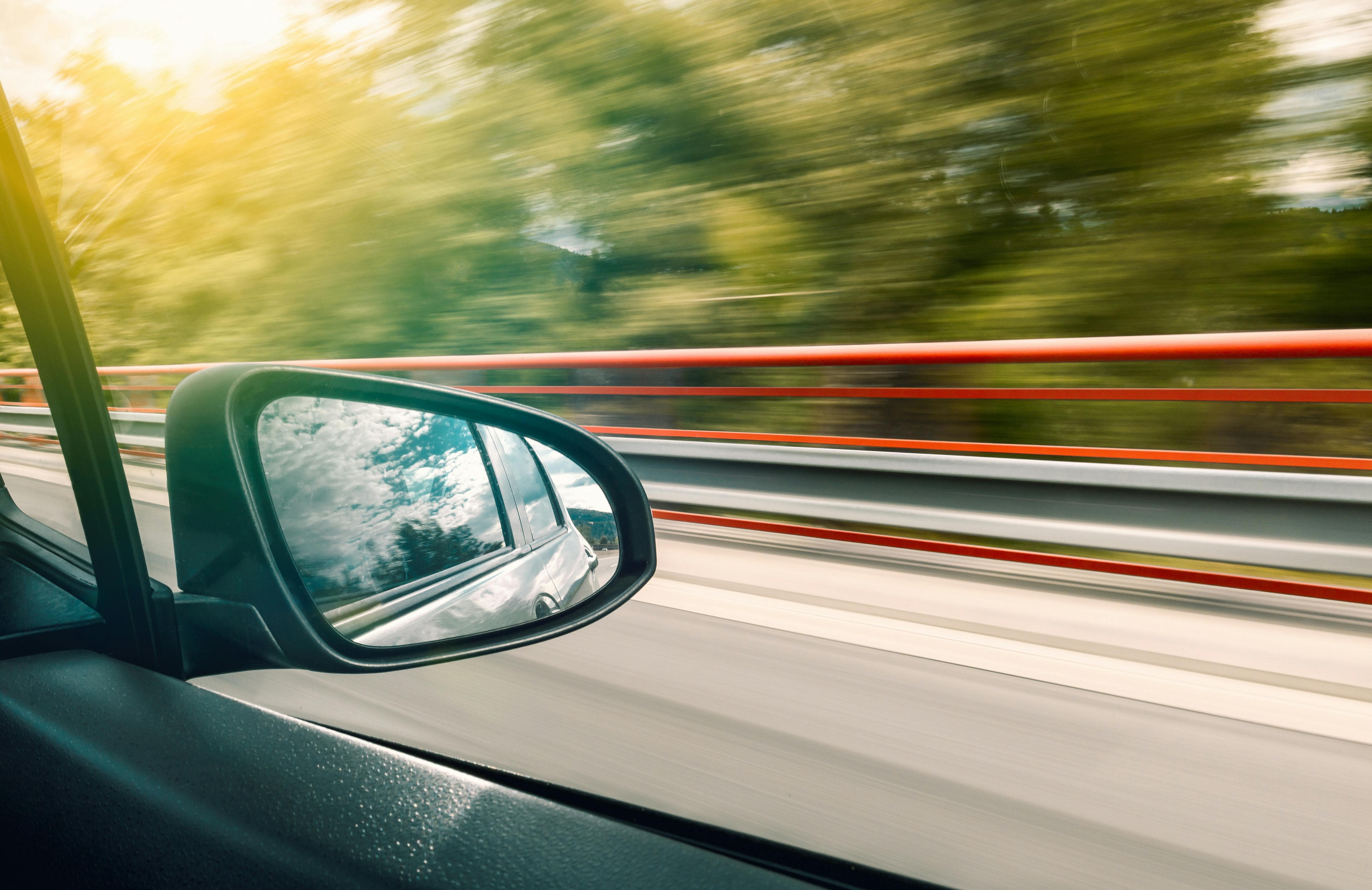Voiture en mouvement sur une route, avec le rétroviseur refletant le ciel.